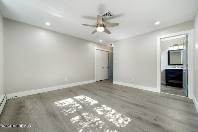 unfurnished bedroom featuring connected bathroom, sink, light wood-type flooring, a closet, and ceiling fan