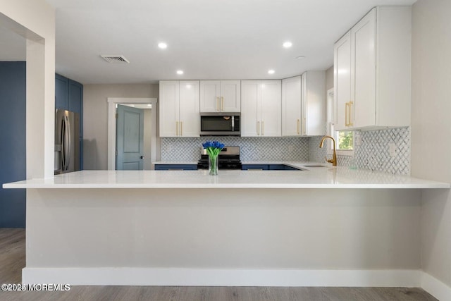 kitchen with appliances with stainless steel finishes, tasteful backsplash, white cabinetry, sink, and kitchen peninsula