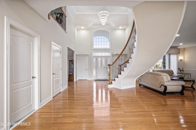 foyer entrance with baseboards, stairway, a high ceiling, crown molding, and light wood-type flooring