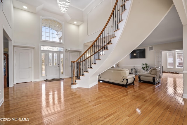 foyer entrance featuring visible vents, stairway, light wood-style floors, ornamental molding, and baseboards