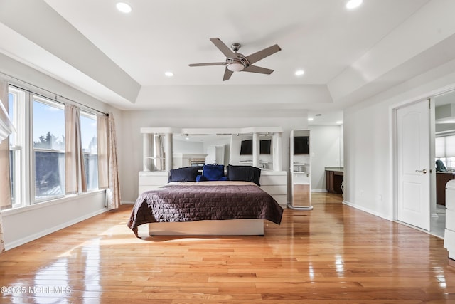 bedroom with light wood-style floors, a tray ceiling, and baseboards