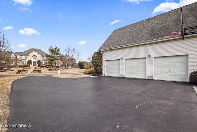 view of side of home with a garage, aphalt driveway, and roof with shingles