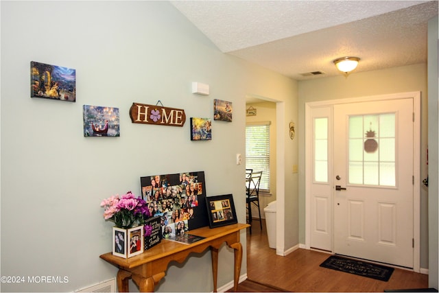 foyer entrance featuring visible vents, a textured ceiling, baseboards, and wood finished floors