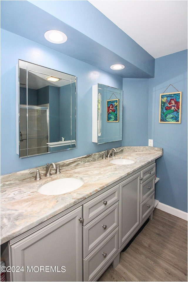 full bathroom with double vanity, a sink, baseboards, and wood finished floors