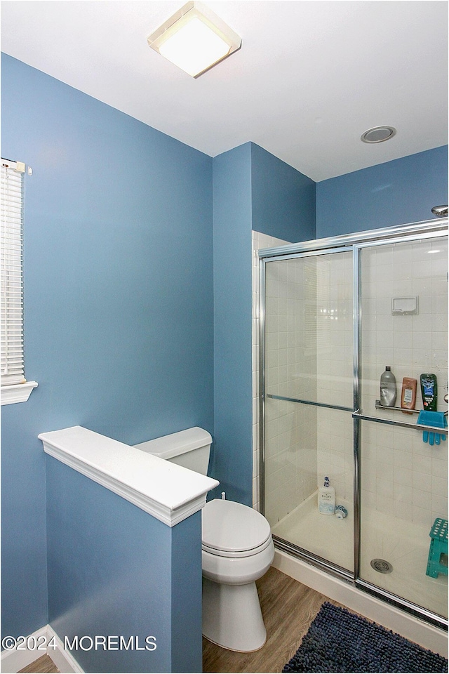 bathroom with tiled shower, wood finished floors, and toilet