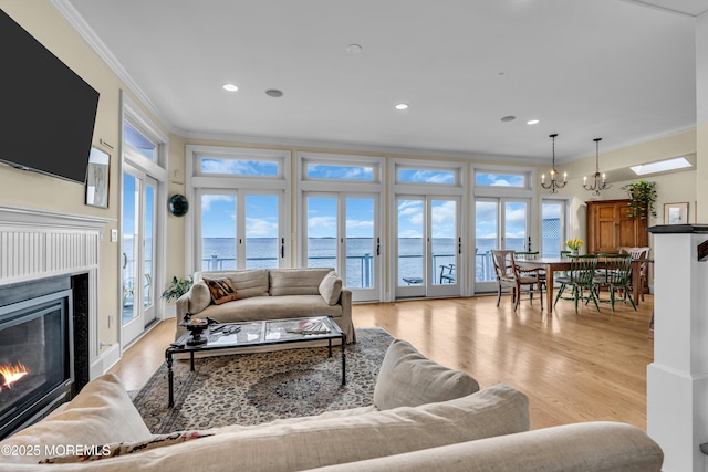 living area with a chandelier, a water view, ornamental molding, light wood finished floors, and a glass covered fireplace