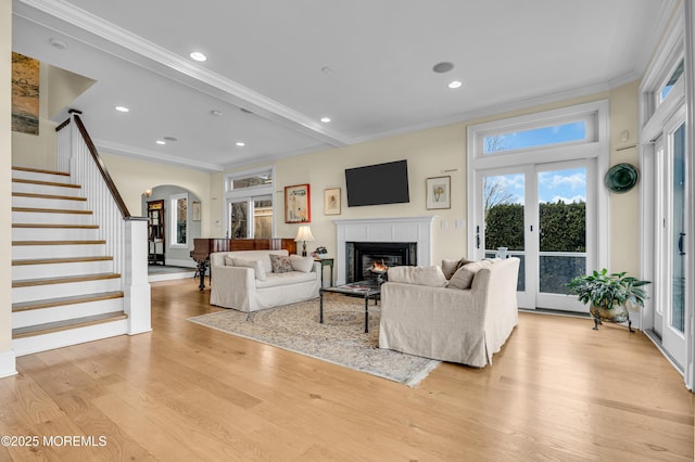 living area with light wood finished floors, arched walkways, a glass covered fireplace, stairs, and crown molding