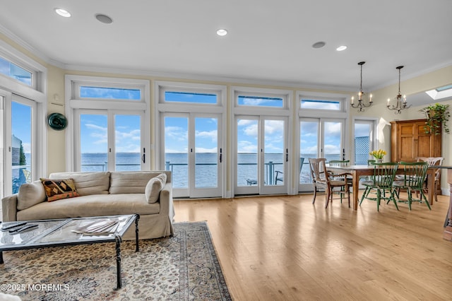 living room featuring a water view, an inviting chandelier, crown molding, light wood-type flooring, and recessed lighting