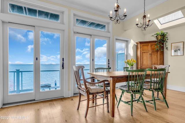 dining room featuring baseboards, a water view, crown molding, light wood-style floors, and a chandelier