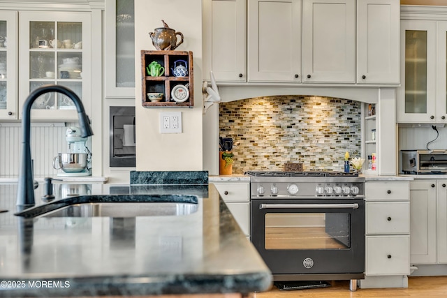 kitchen featuring high end stainless steel range, decorative backsplash, glass insert cabinets, white cabinets, and a sink