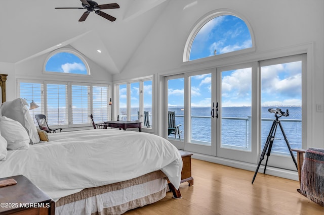 bedroom with high vaulted ceiling, a water view, light wood-style floors, access to outside, and french doors