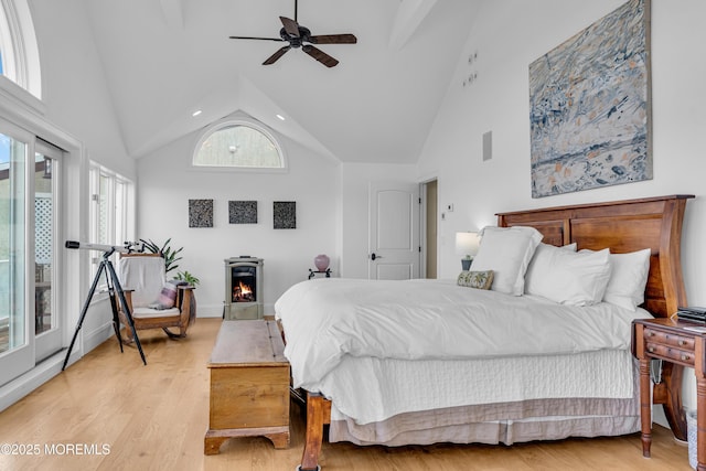 bedroom with a lit fireplace, high vaulted ceiling, a ceiling fan, and light wood-style floors