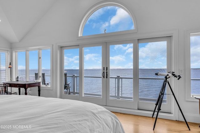 bedroom with lofted ceiling, a water view, wood finished floors, and access to exterior