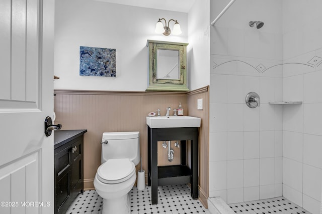 bathroom with toilet, vanity, a tile shower, and wainscoting