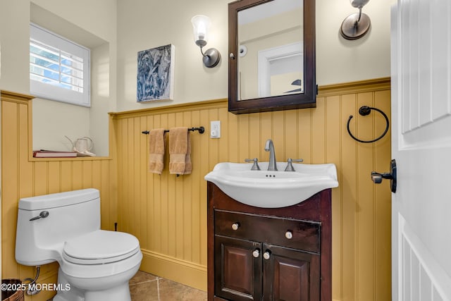 half bath featuring a wainscoted wall, vanity, toilet, and tile patterned floors