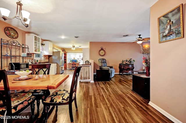 dining space with ceiling fan with notable chandelier, sink, and hardwood / wood-style floors