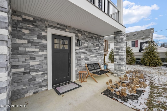 snow covered property entrance featuring a porch and a balcony