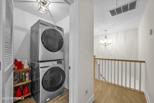 washroom featuring an inviting chandelier, stacked washer and dryer, and light wood-type flooring