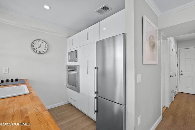 kitchen with light wood finished floors, stainless steel appliances, visible vents, ornamental molding, and white cabinetry