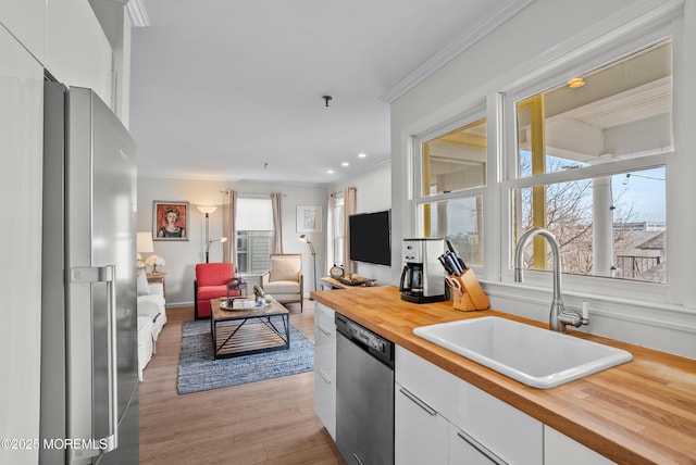 kitchen featuring stainless steel appliances, a sink, white cabinets, open floor plan, and ornamental molding