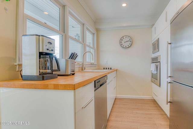 kitchen with light countertops, appliances with stainless steel finishes, ornamental molding, white cabinets, and a sink