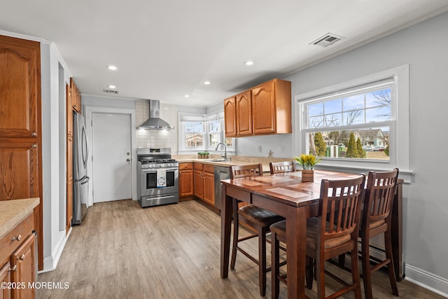 kitchen with visible vents, wall chimney range hood, light countertops, appliances with stainless steel finishes, and a sink