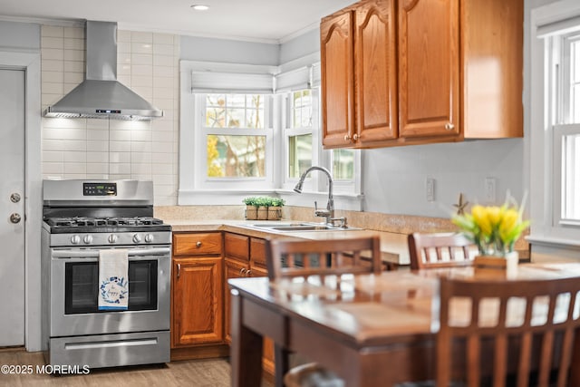 kitchen with stainless steel range with gas stovetop, ornamental molding, a sink, light countertops, and wall chimney exhaust hood