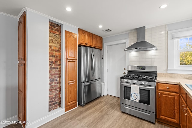 kitchen with light wood finished floors, appliances with stainless steel finishes, ornamental molding, and wall chimney range hood