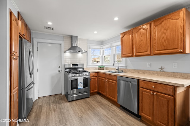 kitchen with visible vents, a sink, stainless steel appliances, wall chimney exhaust hood, and light wood finished floors