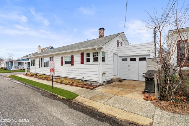 single story home featuring an outbuilding, driveway, an attached garage, a shingled roof, and a chimney