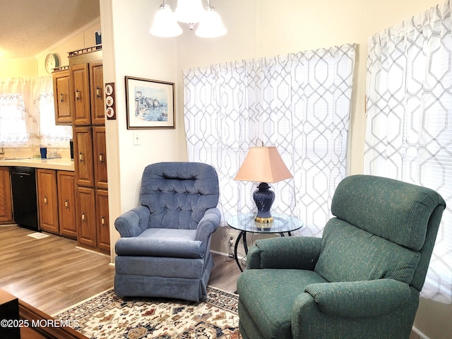 living area with an inviting chandelier, lofted ceiling, crown molding, and light hardwood / wood-style flooring