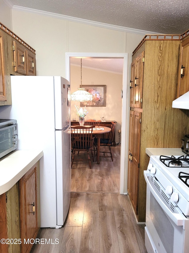 kitchen with hanging light fixtures, hardwood / wood-style flooring, white appliances, crown molding, and a textured ceiling