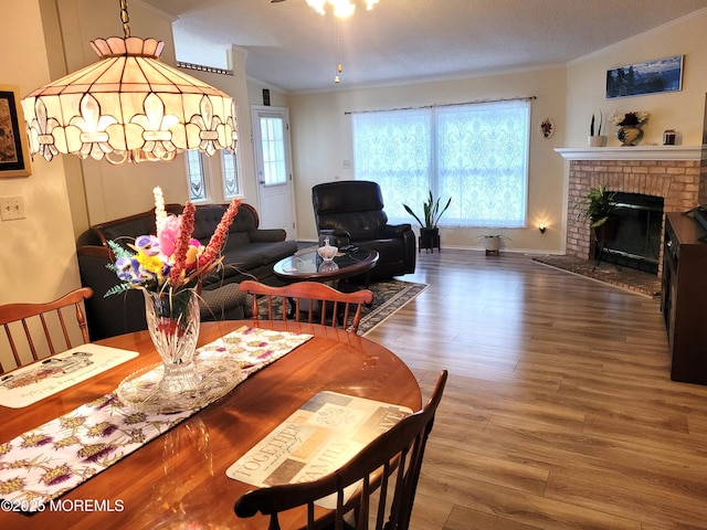 dining space with a fireplace, wood-type flooring, ornamental molding, and vaulted ceiling