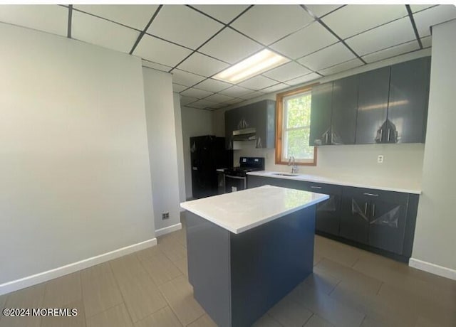 kitchen with sink, black fridge, stainless steel range with electric stovetop, a kitchen island, and a drop ceiling