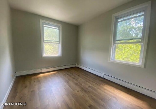 empty room with a baseboard heating unit, hardwood / wood-style flooring, and a healthy amount of sunlight