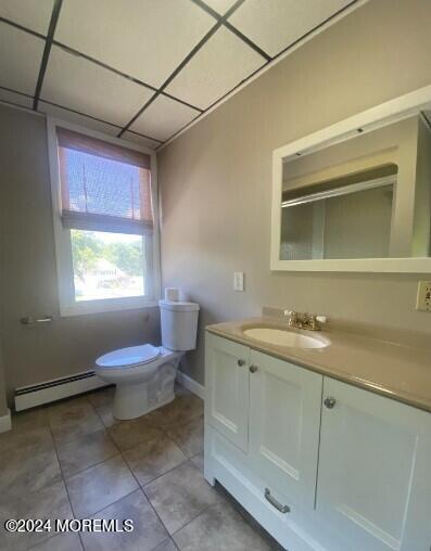 bathroom with vanity, baseboard heating, toilet, a drop ceiling, and tile patterned floors