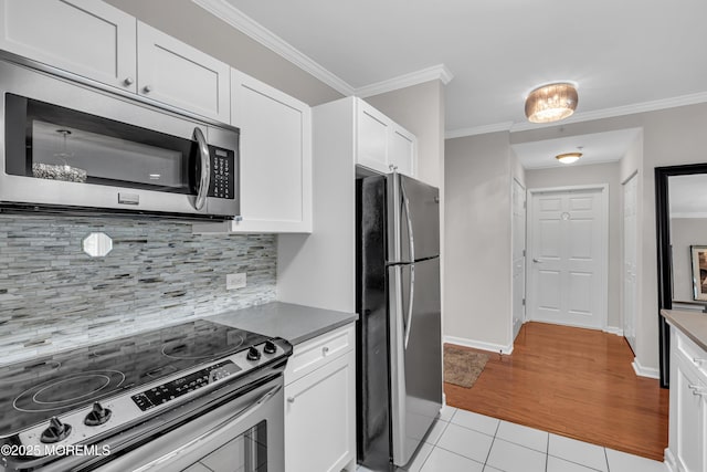 kitchen with white cabinetry, ornamental molding, stainless steel appliances, and light tile patterned floors