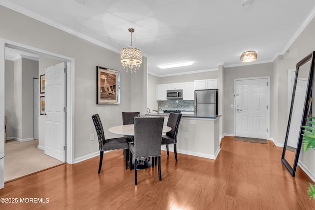 dining area featuring crown molding, sink, a chandelier, and light hardwood / wood-style floors