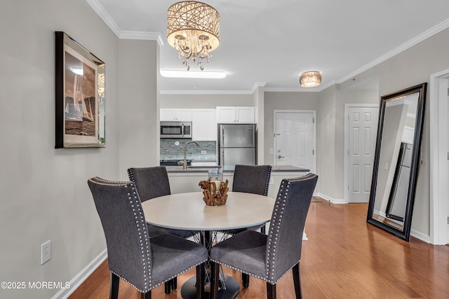 dining space with ornamental molding, sink, a chandelier, and hardwood / wood-style floors