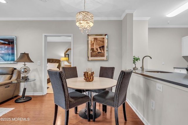 dining area with an inviting chandelier, ornamental molding, light hardwood / wood-style floors, and sink