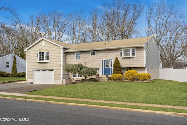 raised ranch featuring aphalt driveway, roof with shingles, a front yard, fence, and a garage