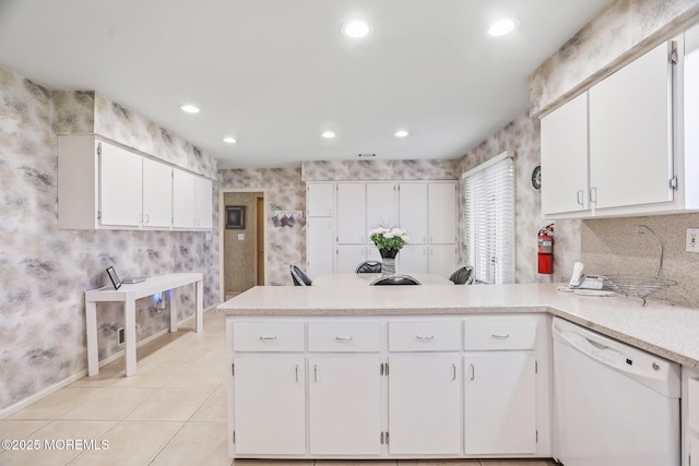 kitchen with wallpapered walls, light tile patterned floors, white cabinets, dishwasher, and a peninsula