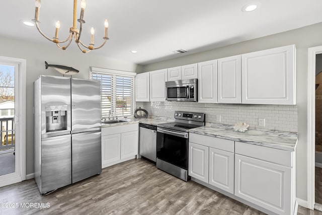 kitchen with light wood finished floors, a sink, stainless steel appliances, white cabinetry, and backsplash