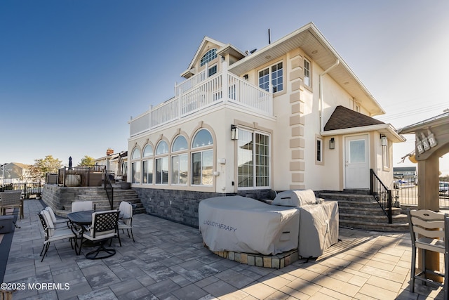 rear view of house with outdoor dining space, a balcony, a patio area, and stucco siding