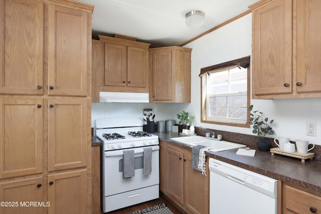 kitchen with under cabinet range hood, white appliances, a sink, dark countertops, and crown molding