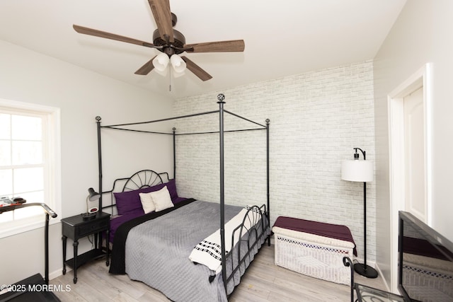 bedroom featuring ceiling fan, brick wall, and light wood-type flooring