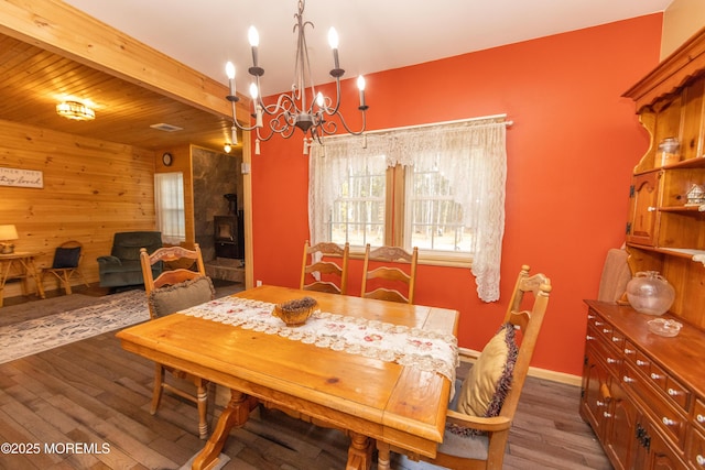 dining room with an inviting chandelier, beam ceiling, dark wood-type flooring, and wooden walls