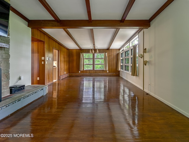 unfurnished living room featuring beam ceiling, hardwood / wood-style flooring, wooden walls, and baseboards