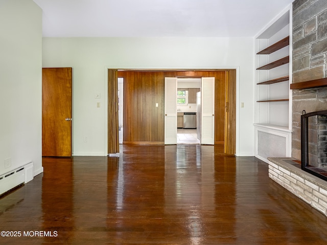 unfurnished living room featuring built in features, a large fireplace, wood finished floors, and baseboards