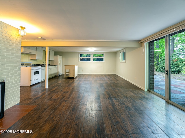 unfurnished living room with dark wood-type flooring, baseboards, and a brick fireplace